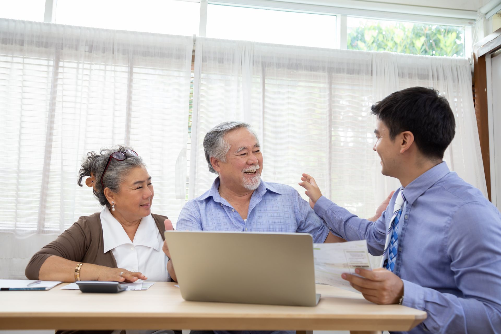 Senior couple reviewing paperwork with a financial advisor at a table with a laptop.