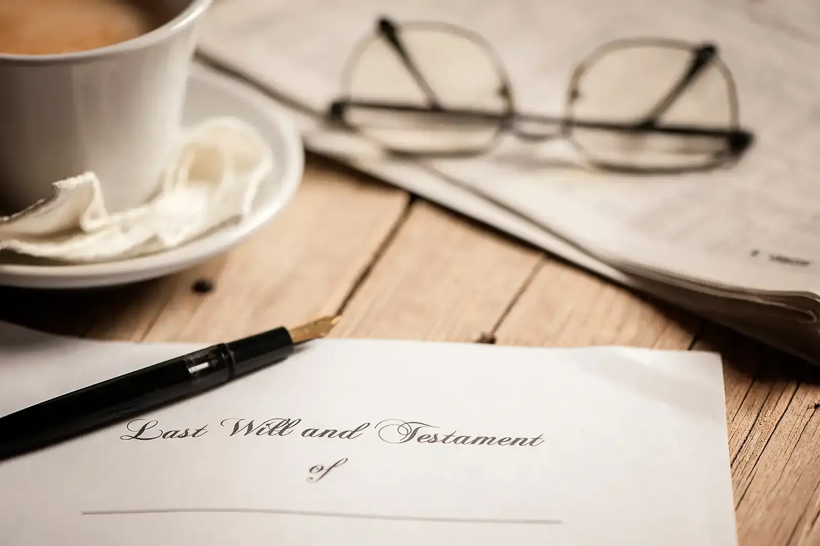 Will document with pen, glasses, coffee cup, and newspaper on a wooden table.