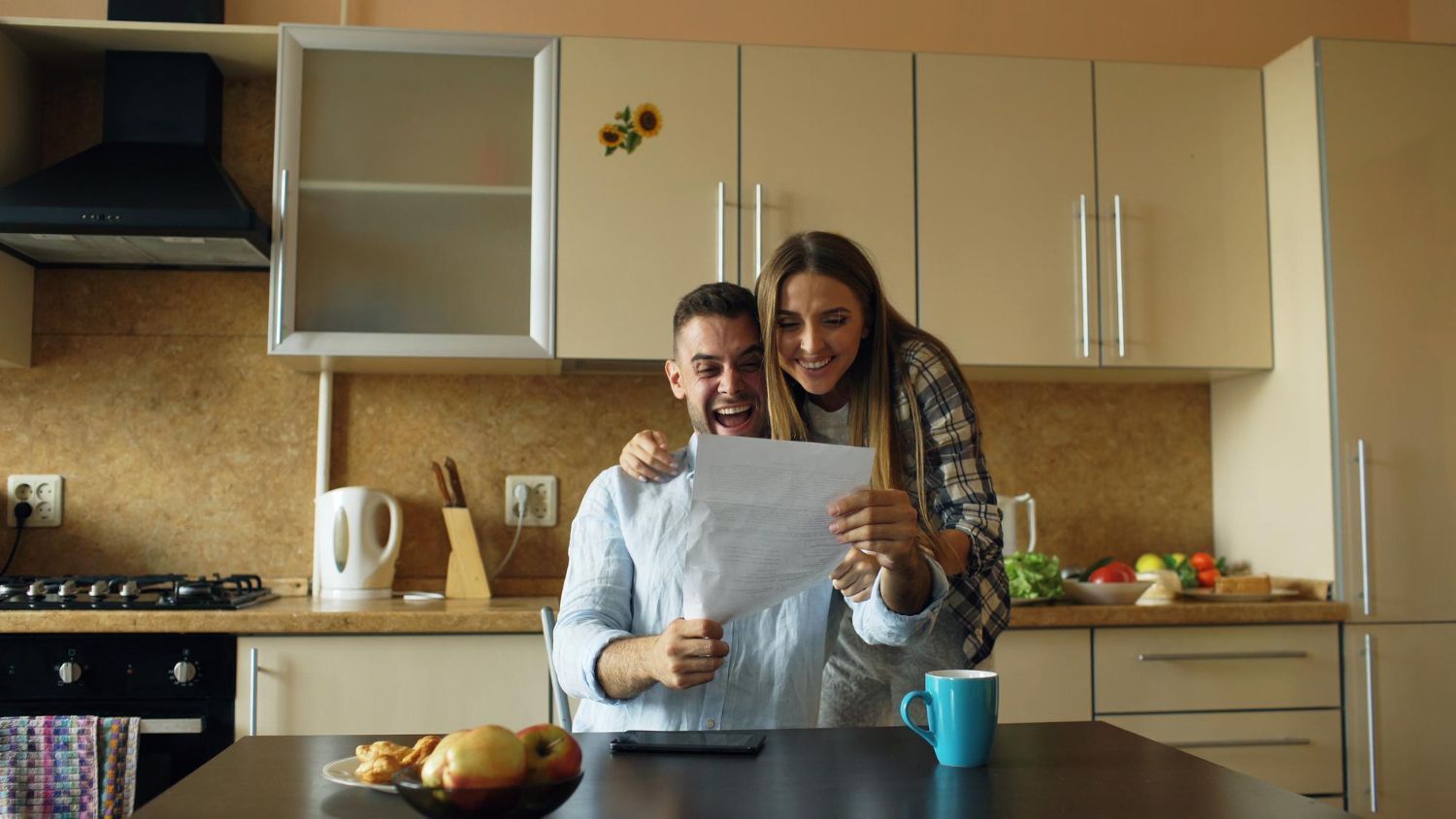 Two people smiling while looking at a paper together at a kitchen table.
