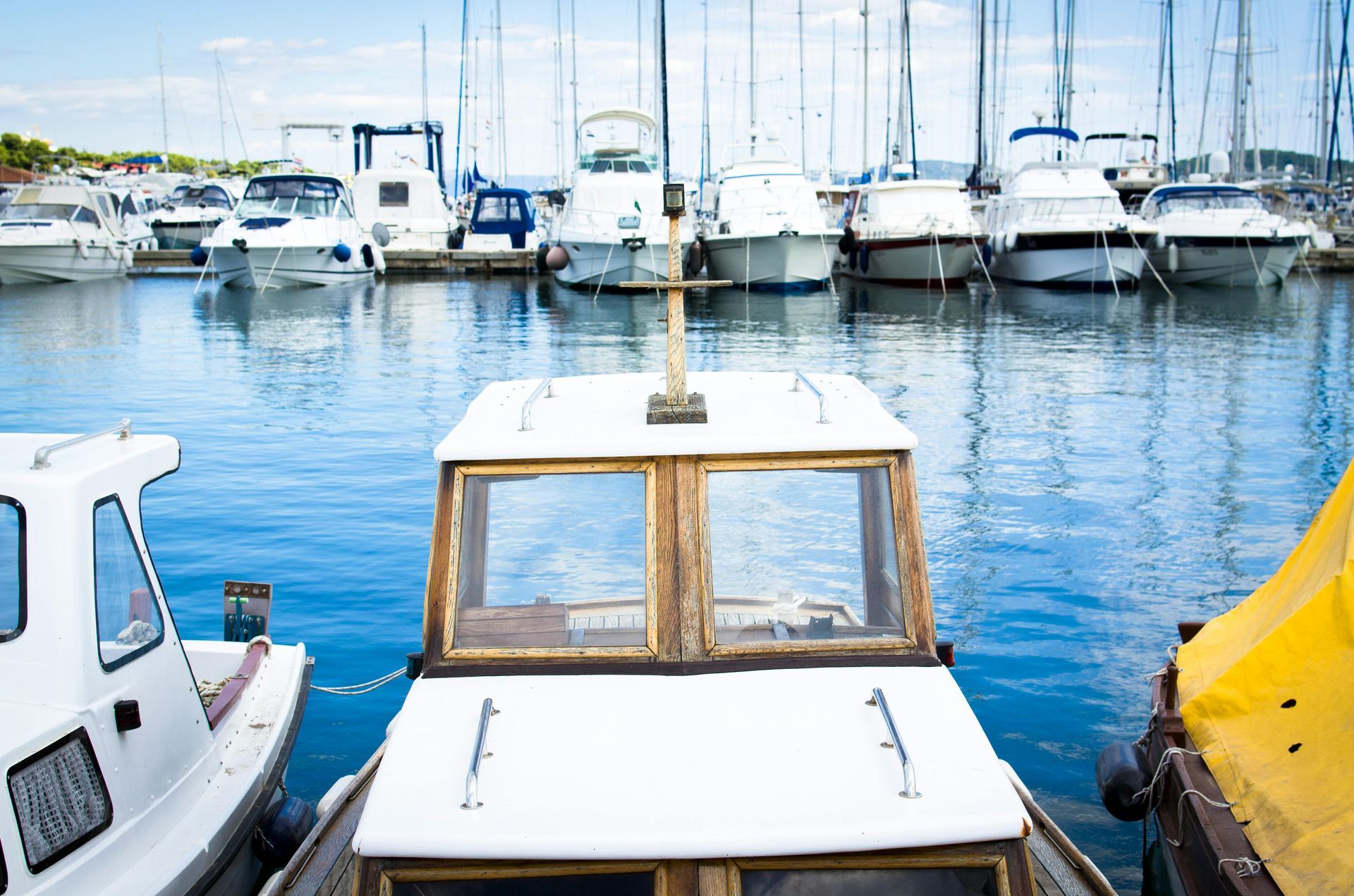 A close-up view of the white cabin and windshield of a small boat docked in a harbor filled with various boats.