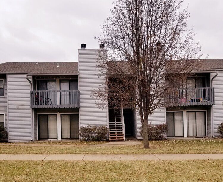 Apartment building with balconies and sliding glass doors; bare tree in front on a cloudy day.