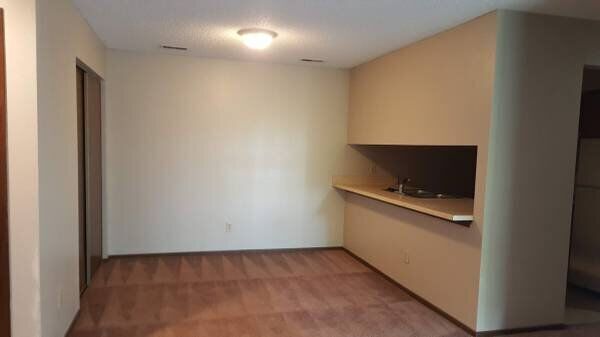 Empty room with built-in counter, brown floors, and off-white walls.