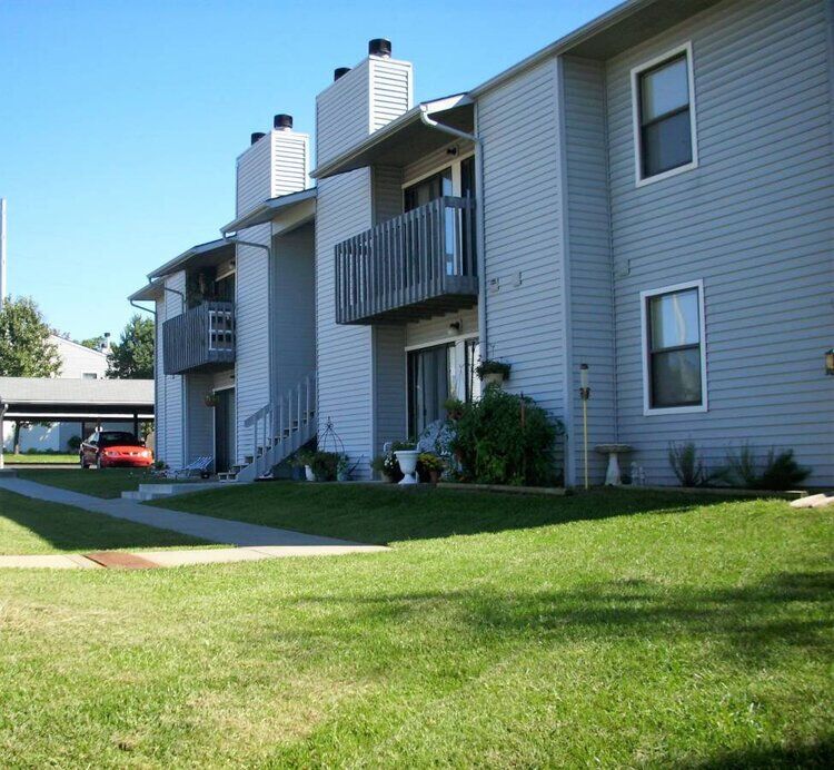 Apartment building with light blue siding, balconies, and green lawn on a sunny day.