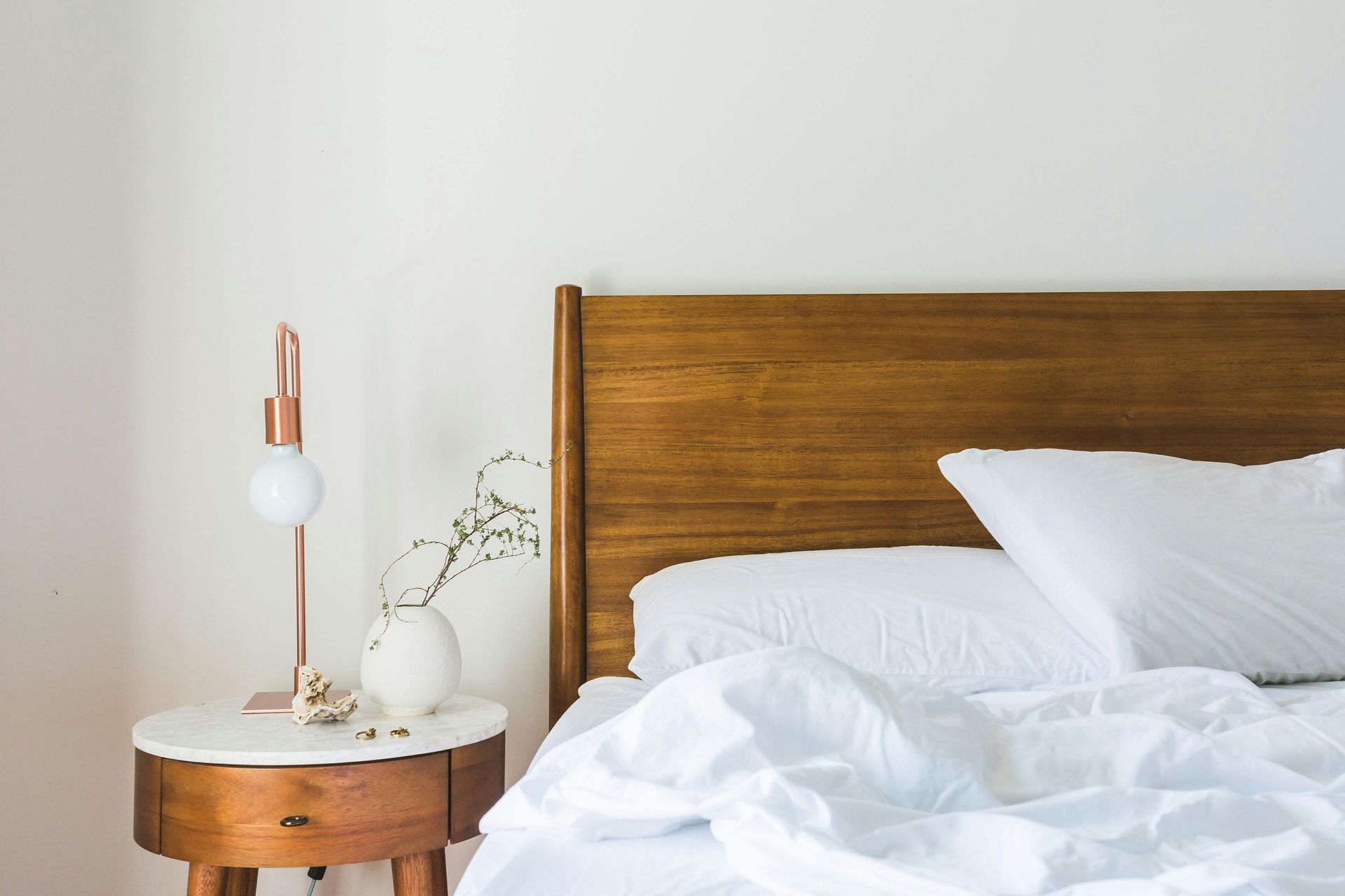 Bed with wooden headboard and white linens, a nightstand with lamp and vase.