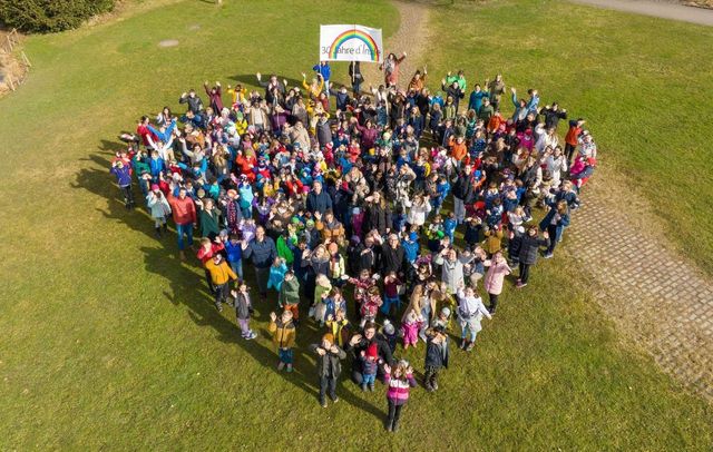 A large group of people are standing in a field in the shape of a heart.