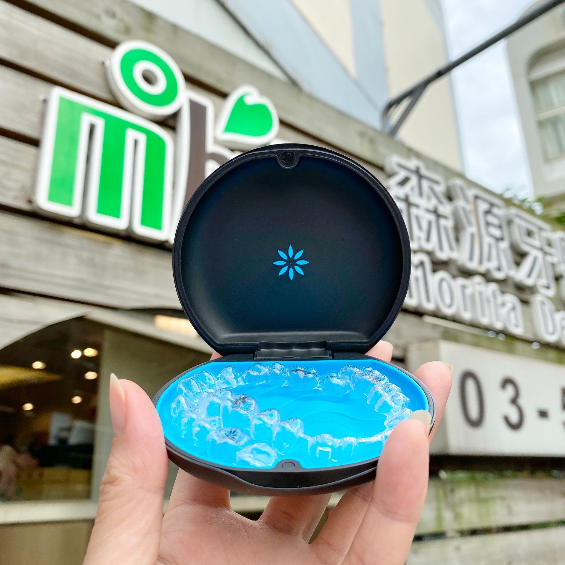 A person is holding an invisalign case in front of a building.