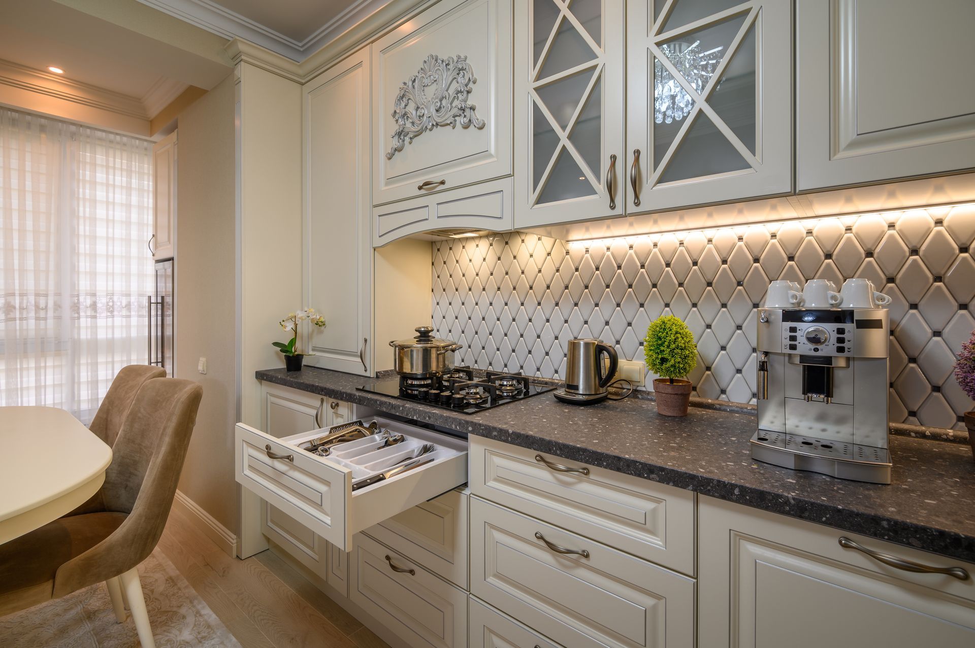 A modern kitchen with cream-colored cabinetry, a tiled backsplash, an open utensil drawer, a stove, and a coffee machine.