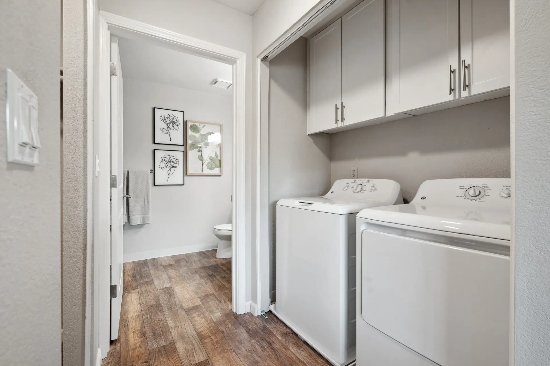 Laundry area with side-by-side washer and dryer and white upper cabinets.