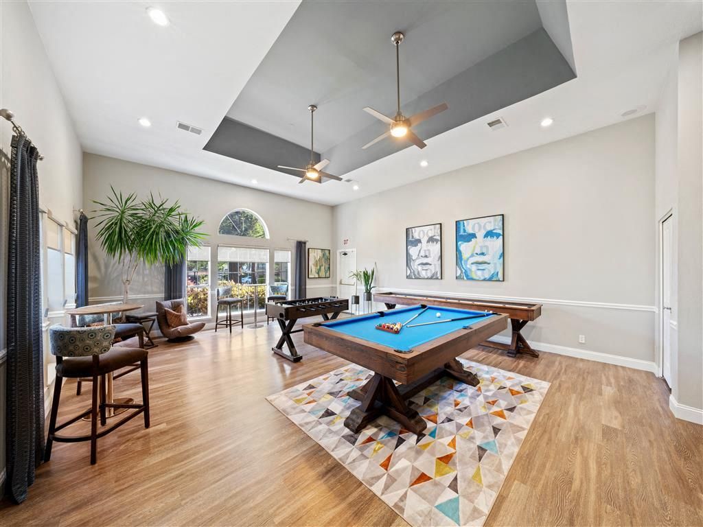Recreation room with two pool tables, seating area, plants, and large windows.