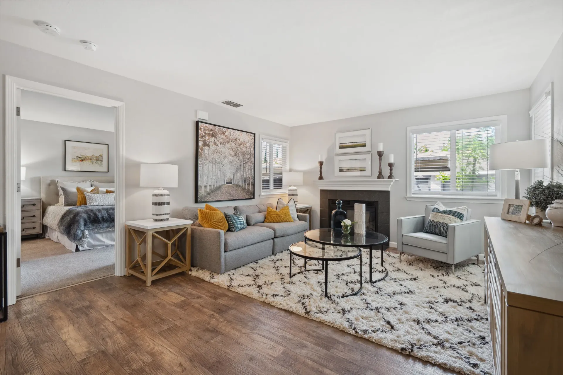 Living room in a modern apartment: gray sofa, coffee tables, fireplace, and large windows.
