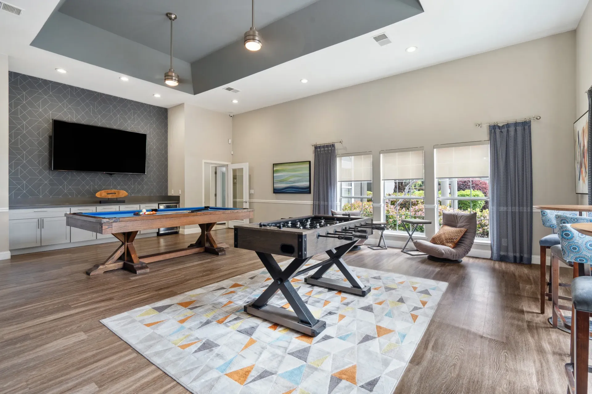 Indoor community recreation room with pool table, foosball table, TV, and seating.