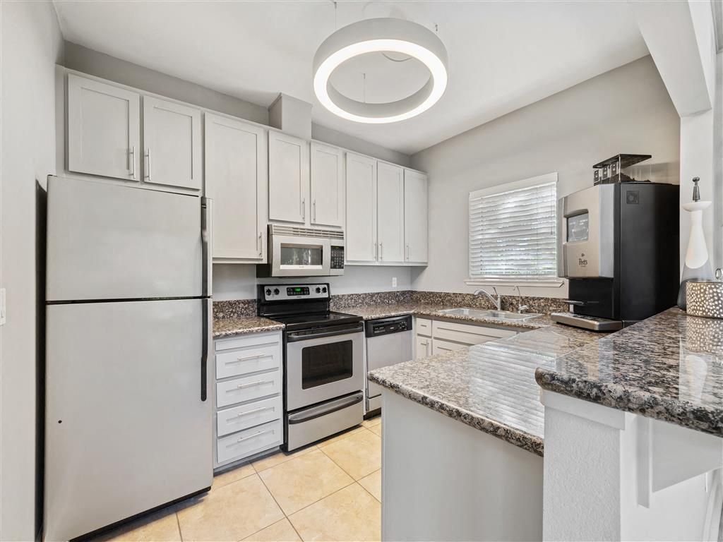 Modern apartment kitchen with white cabinets, granite countertops, and stainless steel appliances.
