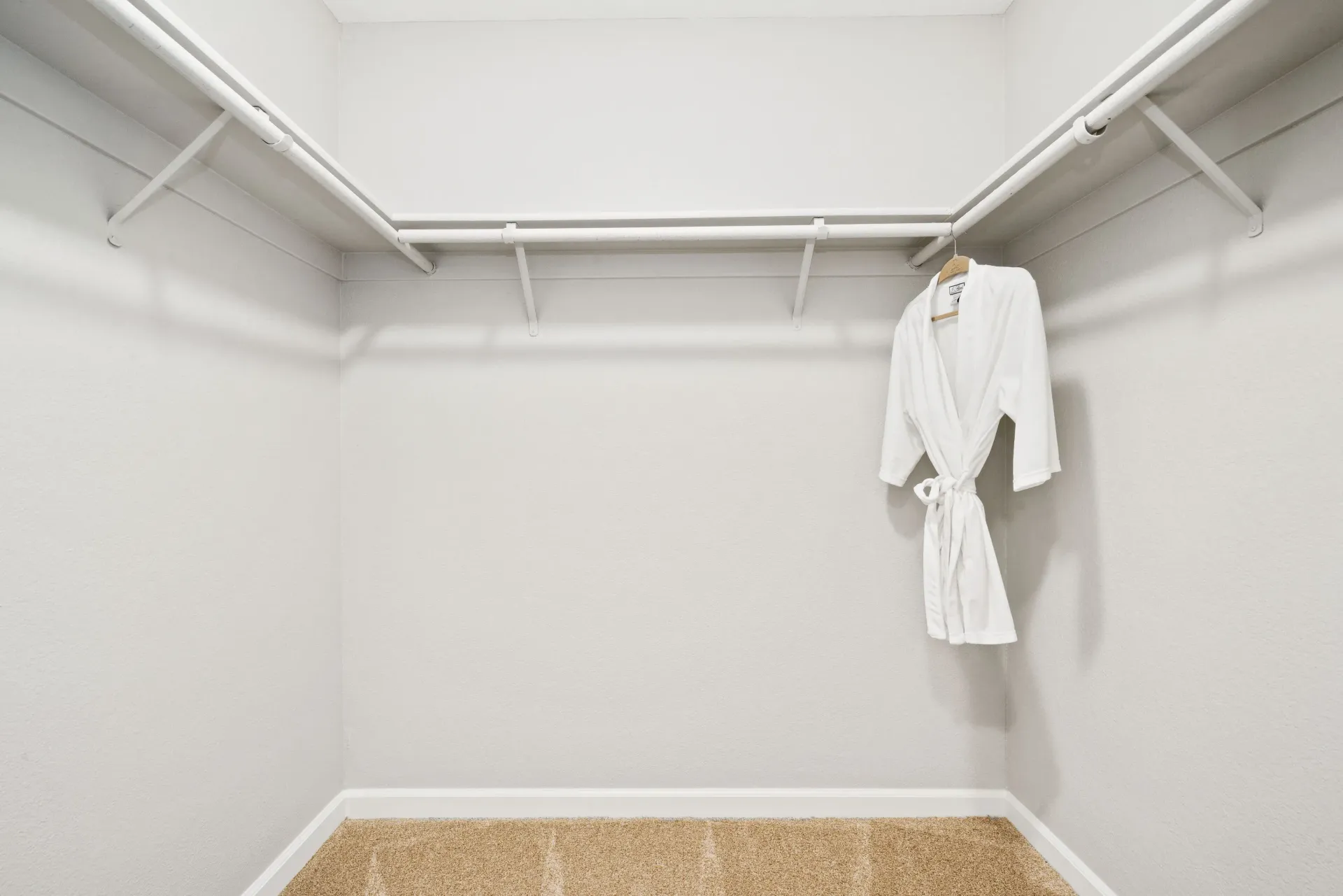 Bright walk-in closet with white rods and a hanging white bathrobe.