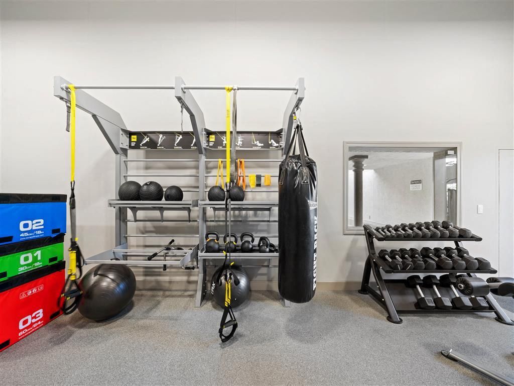 Indoor community gym with weight rack, medicine balls, kettlebells, dumbbells, and a hanging punching bag.