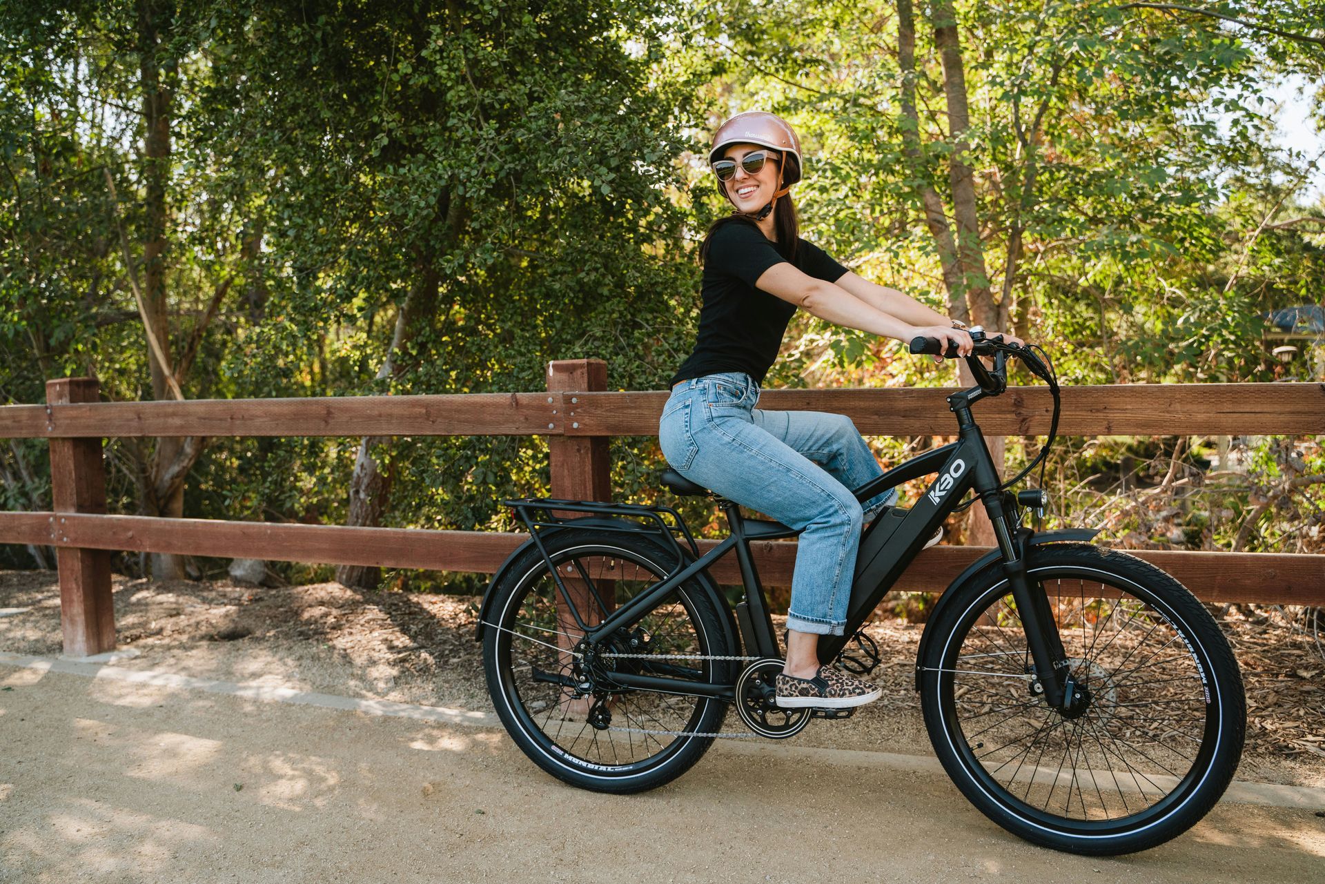 A woman is riding an electric bike next to a wooden fence.