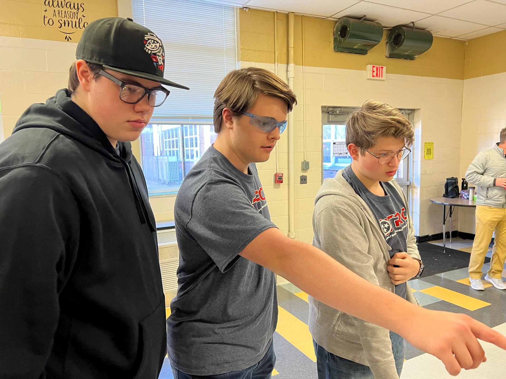 Three young men wearing glasses and a hat are standing in a room.