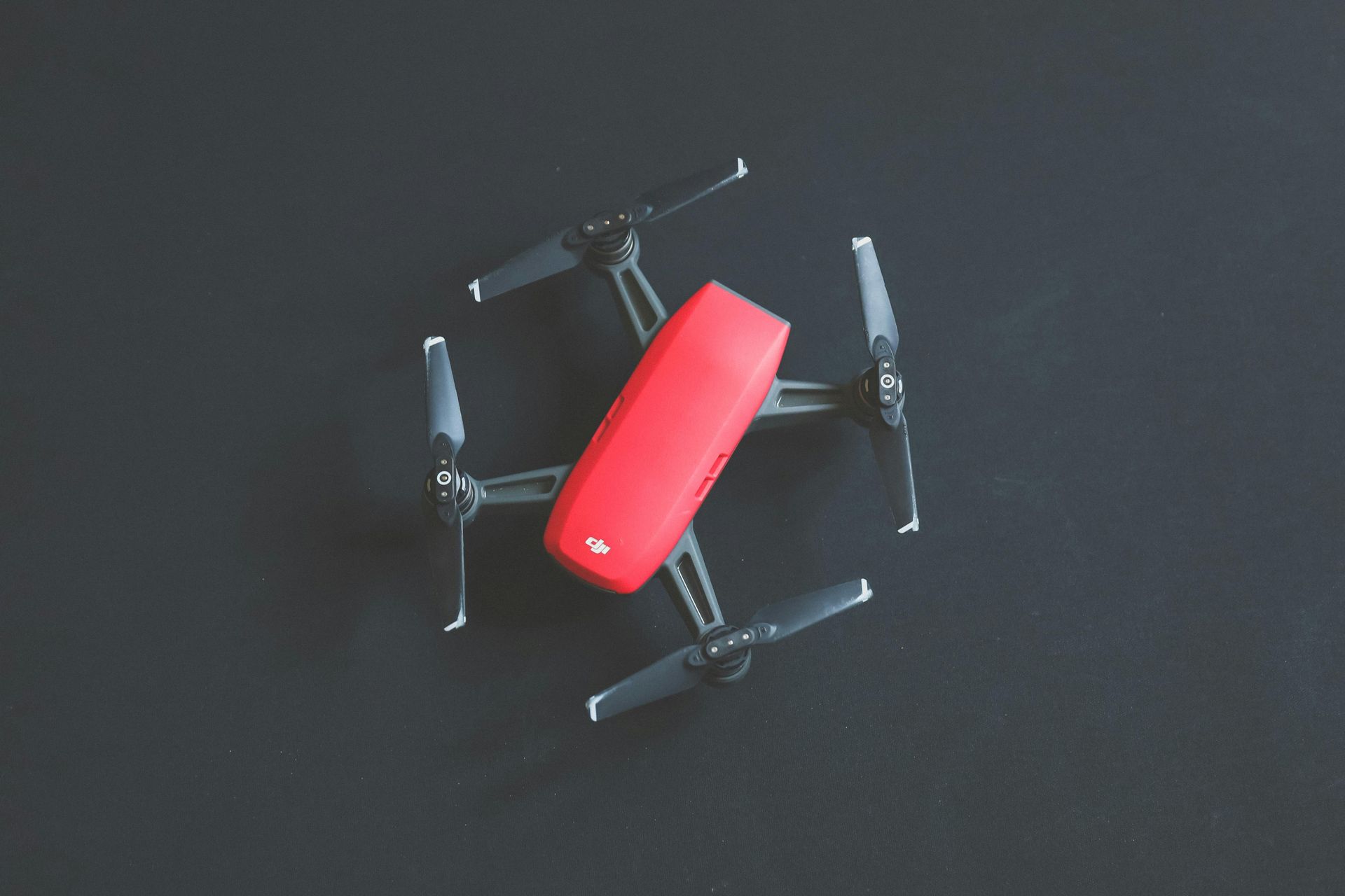 Red and black drone on a dark surface, with four propellers.