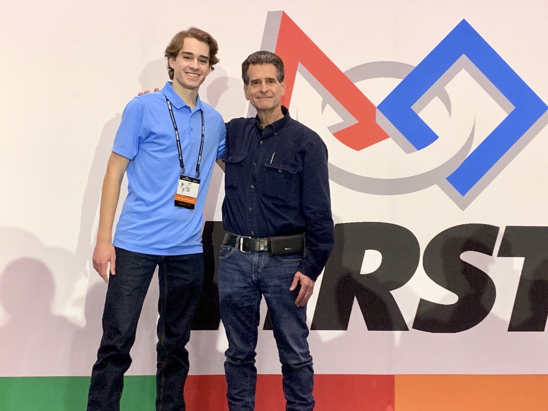 Two men standing in front of a sign that says first