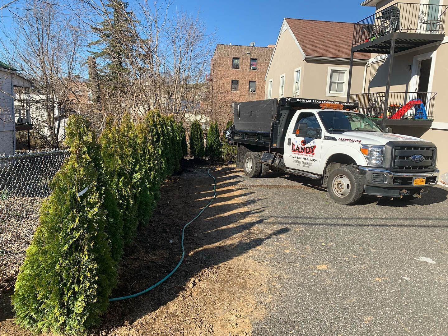 A white dump truck parked near a row of evergreen trees in a gravel driveway.