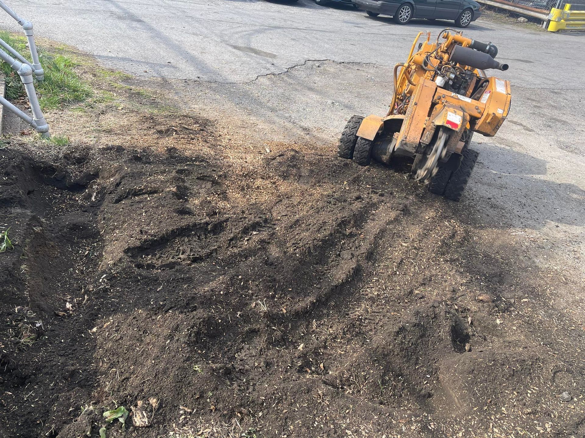 A yellow stump grinder on gravel, with a pile of wood chips and dirt nearby.