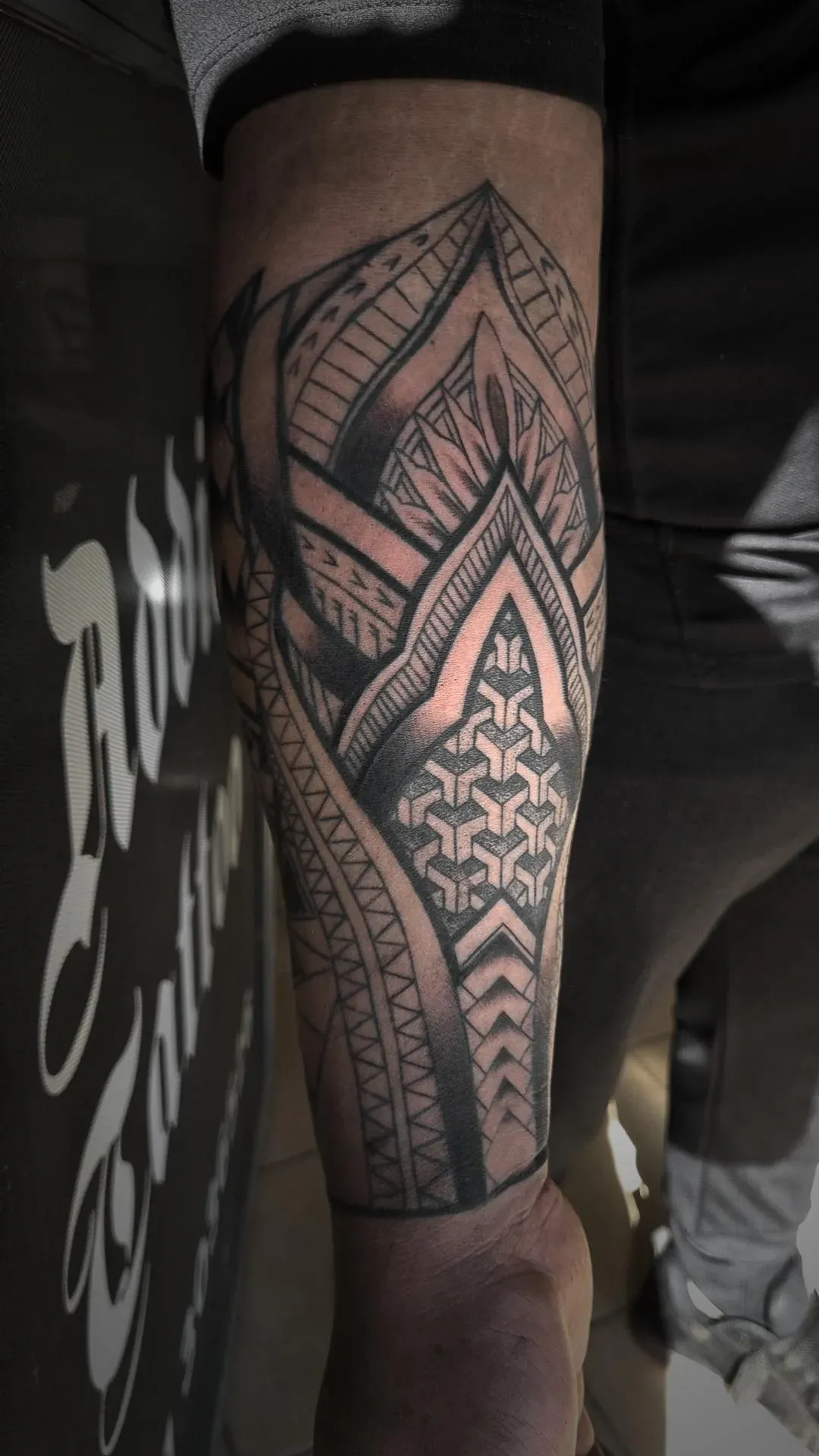 Tatuaje en el antebrazo, intrincado diseño geométrico en negro y gris, estilo tribal.