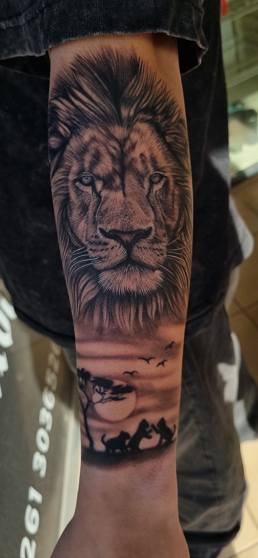 Tatuaje de león en el antebrazo con escena de atardecer de fondo.