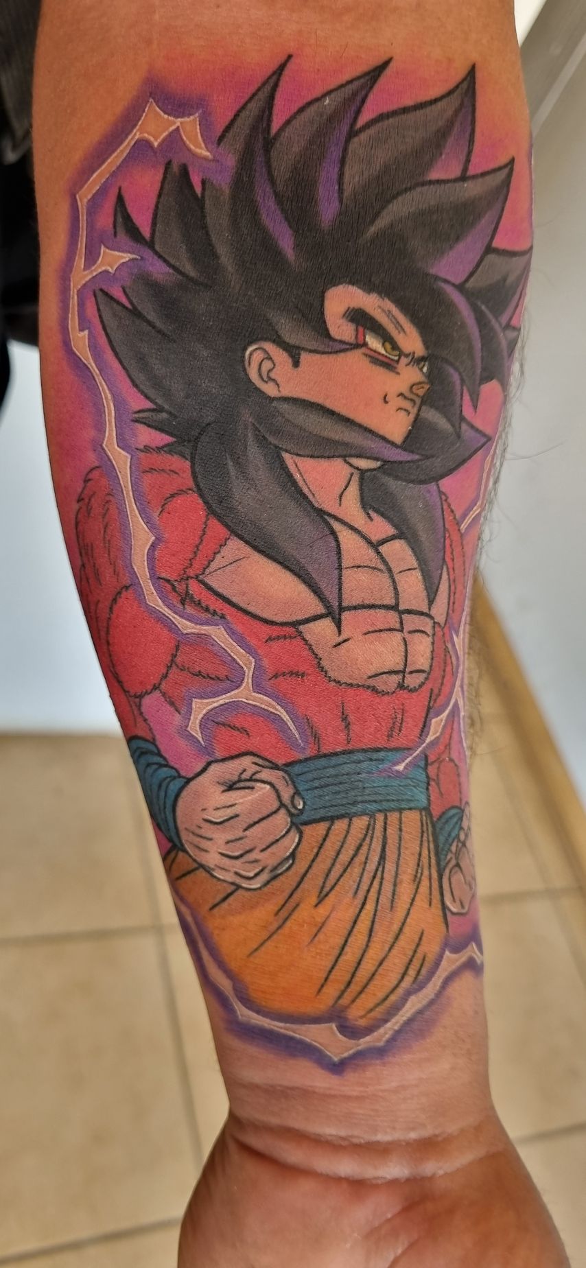 Tatuaje de Goku Super Saiyan 4 de Dragon Ball Z en el antebrazo. Tiene cabello negro y un traje rojo.