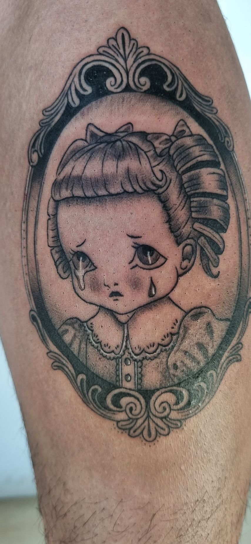 Tatuaje de una niña triste y caricaturesca con lágrimas en un marco ovalado vintage.