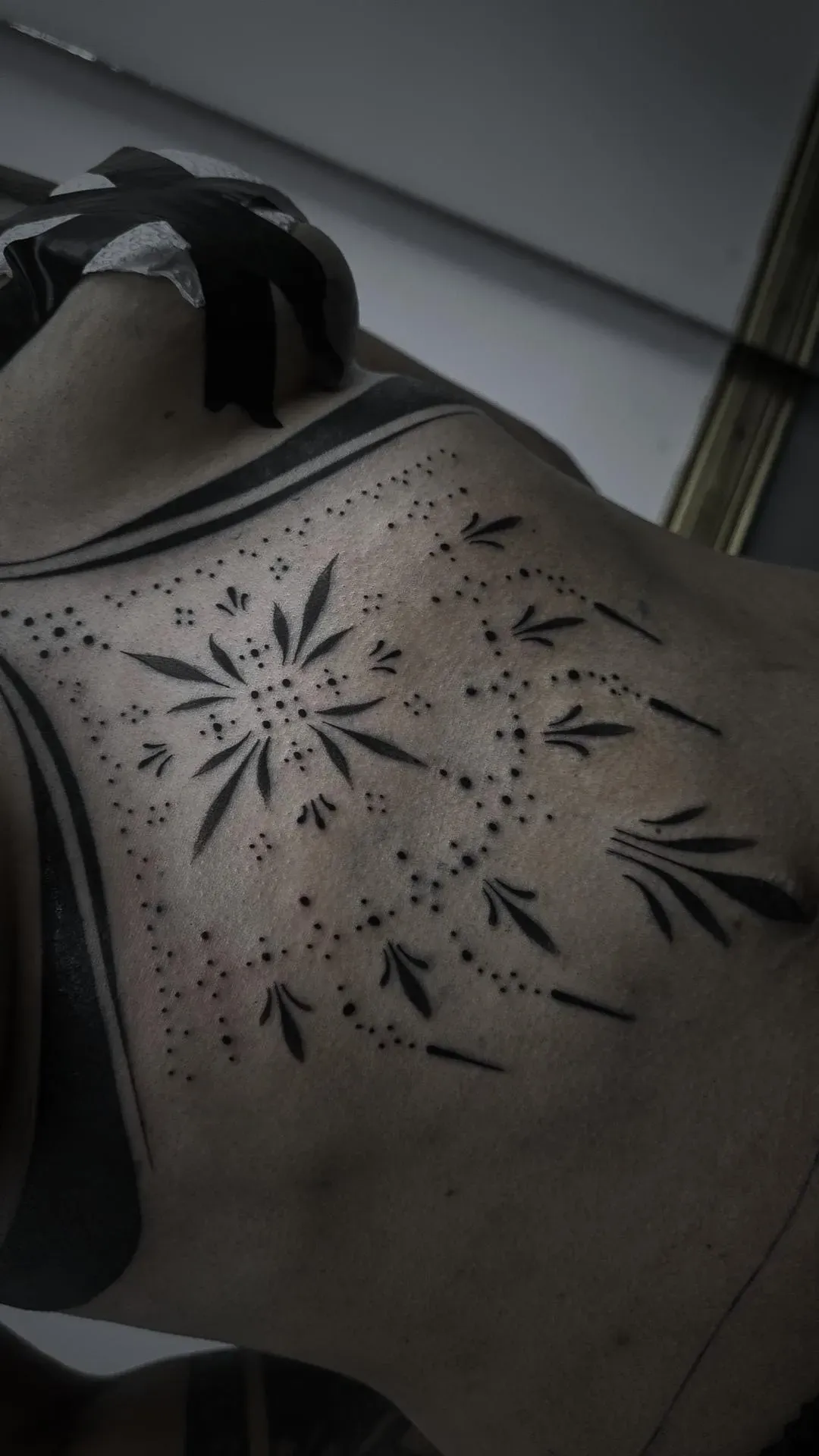 Tatuaje en el torso con diseño geométrico negro con elementos punteados y en forma de hojas.