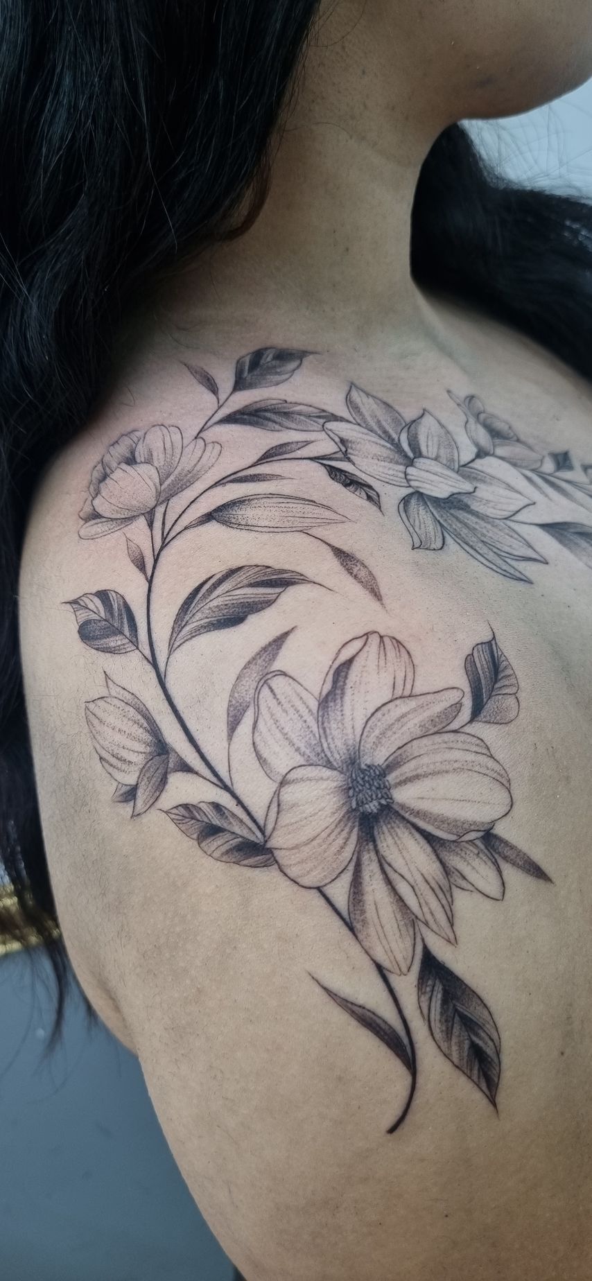 Tatuaje floral negro y gris en el hombro. Flores y hojas tatuadas.