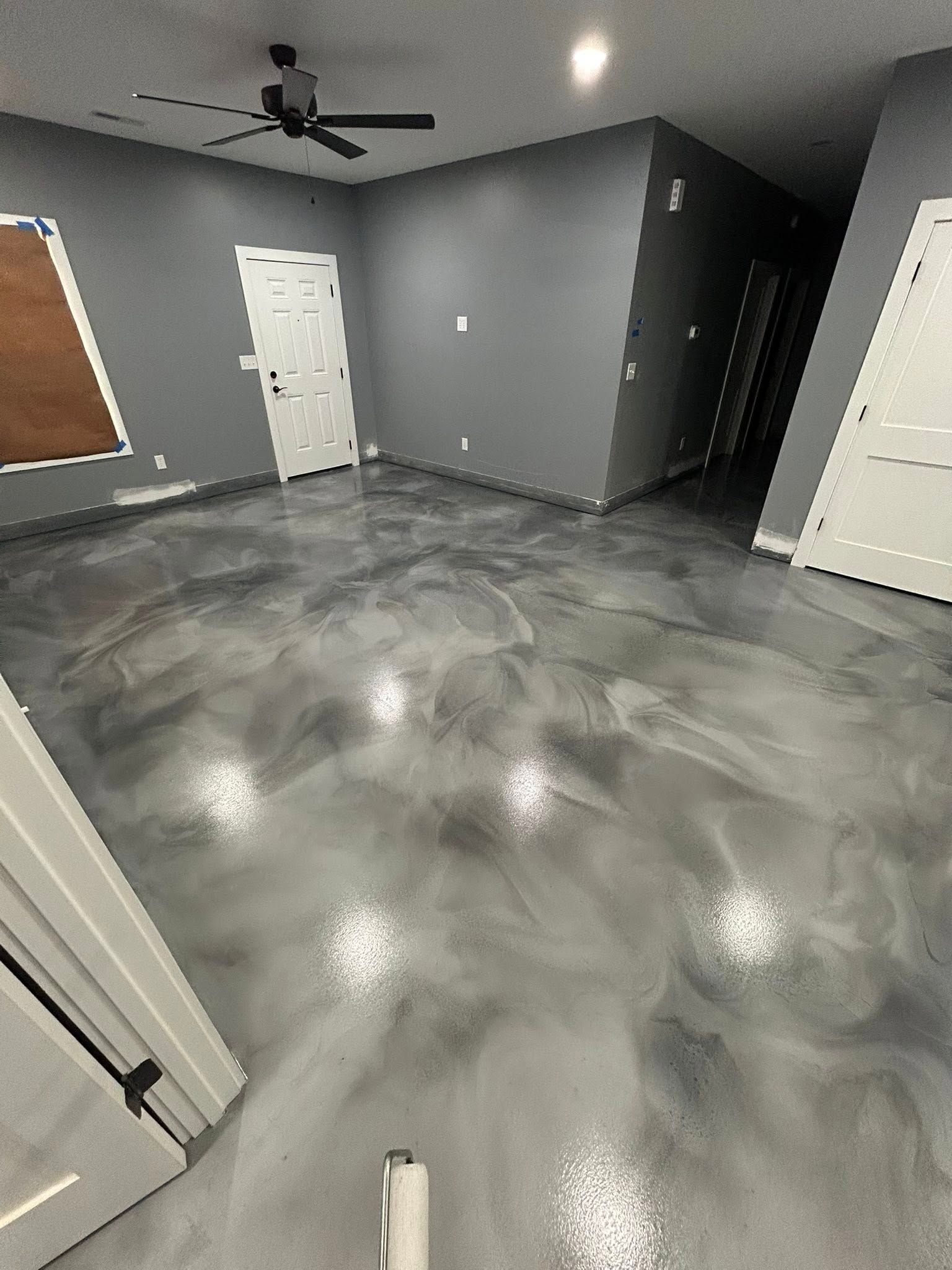 A room with a polished, grey marbled epoxy floor, white doors, and a ceiling fan against dark grey walls.