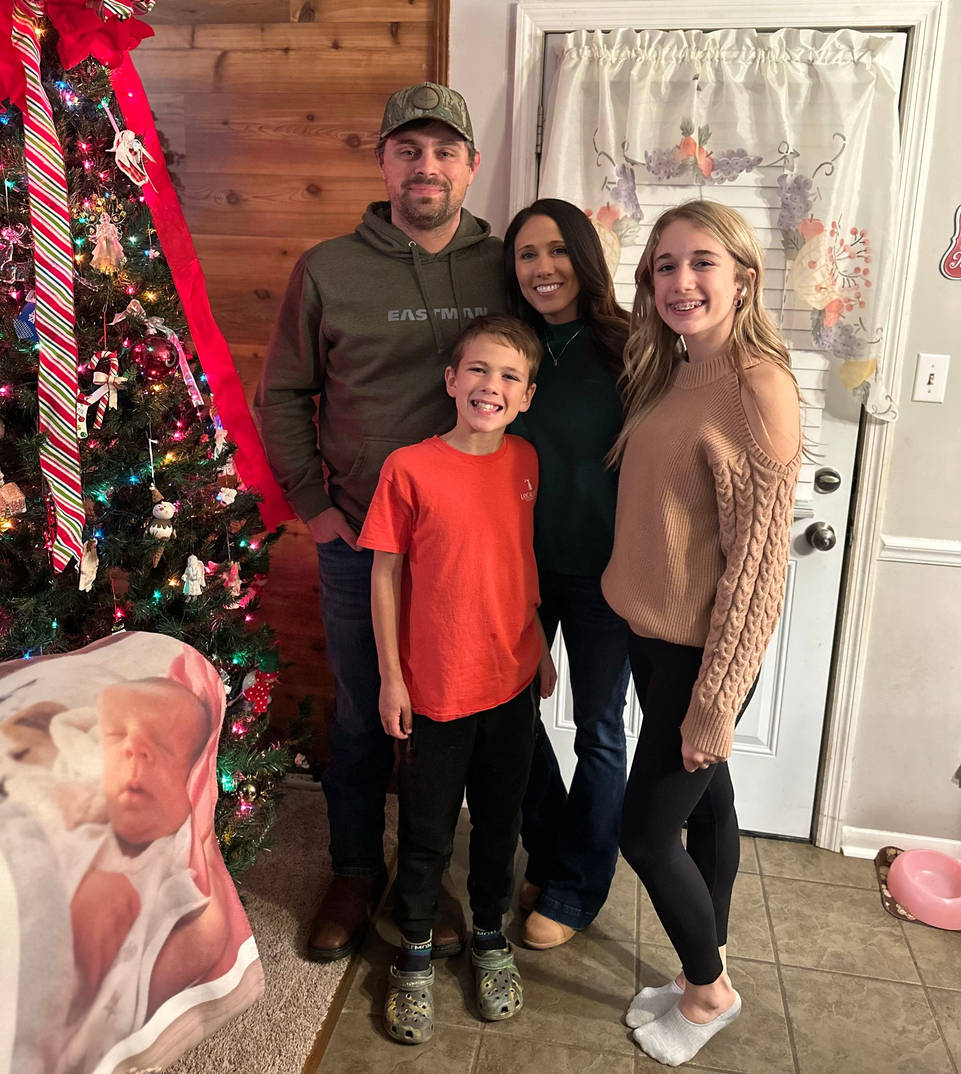 A family poses together in front of a decorated Christmas tree in a home setting.