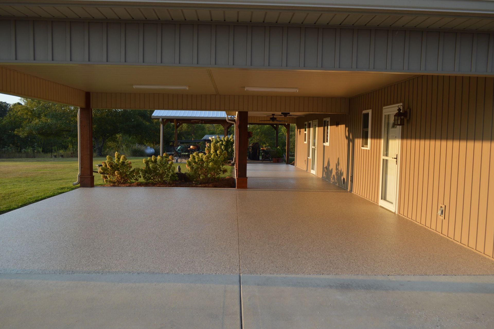 A tan home with a covered porch featuring a decorative, speckled epoxy floor, looking out toward a grassy lawn.