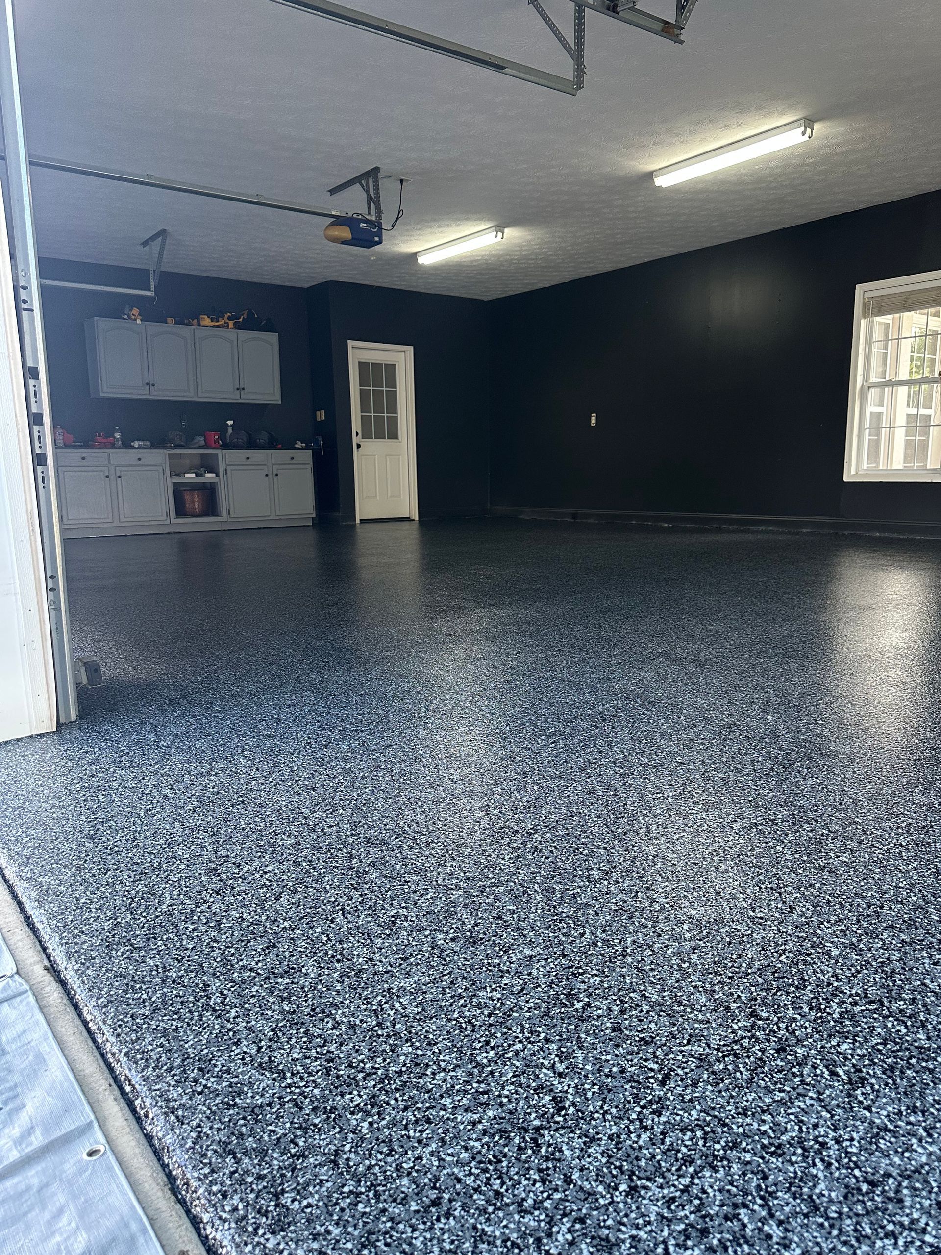 A garage with a speckled, black-and-white epoxy floor, dark painted walls, and bright overhead lighting.