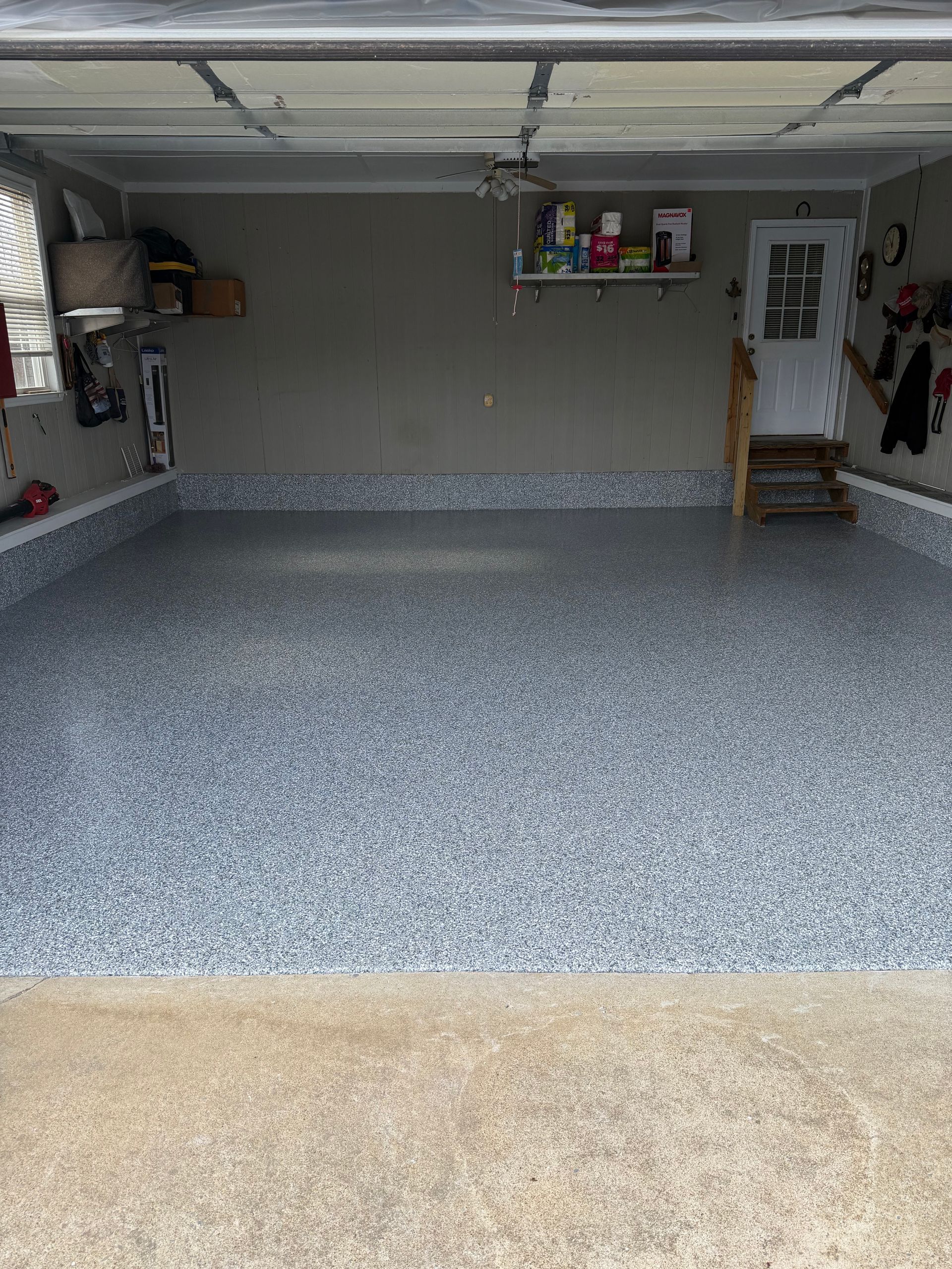 A garage interior featuring a freshly finished, grey and white speckled epoxy floor with a matching low-profile trim.
