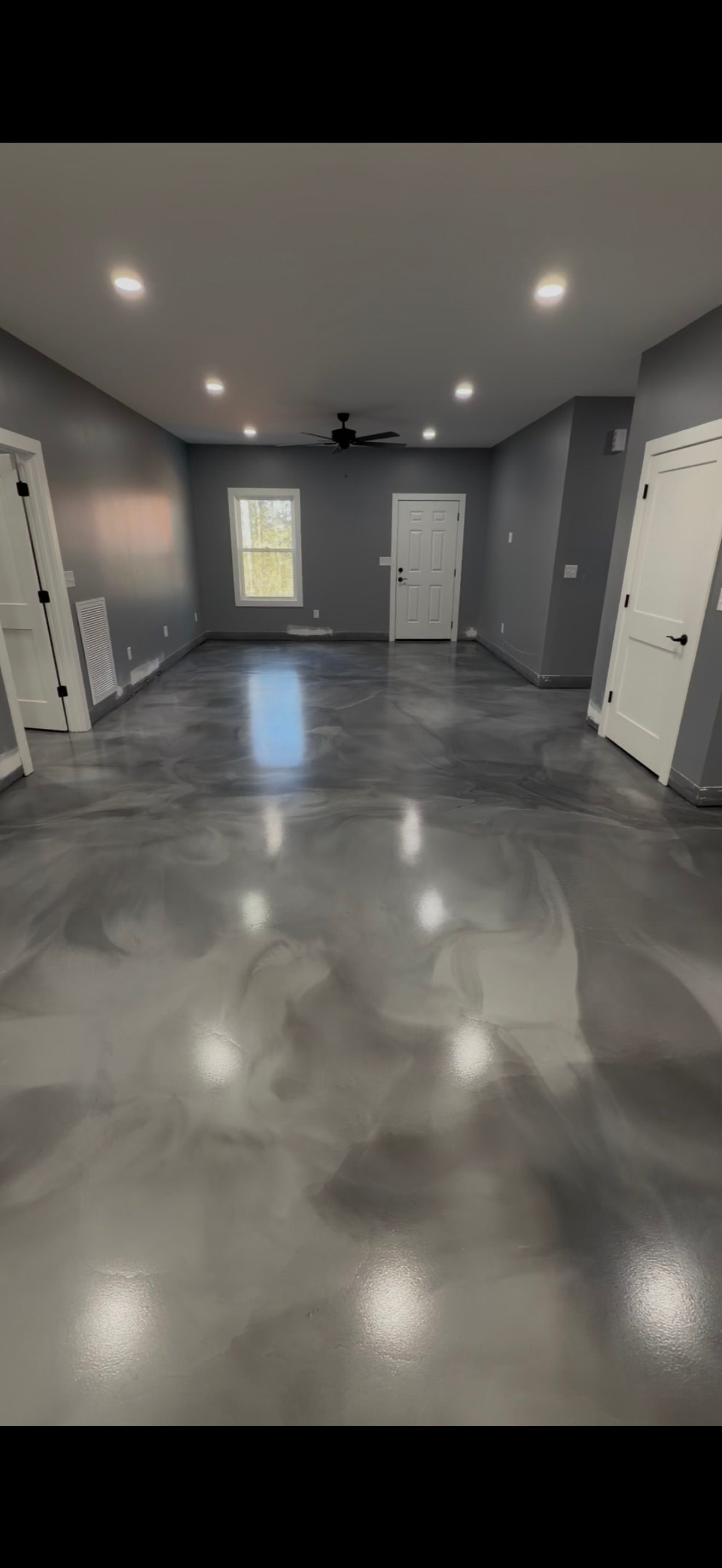 A room with grey walls, white trim, recessed lighting, and a high-gloss, marbled grey epoxy floor.