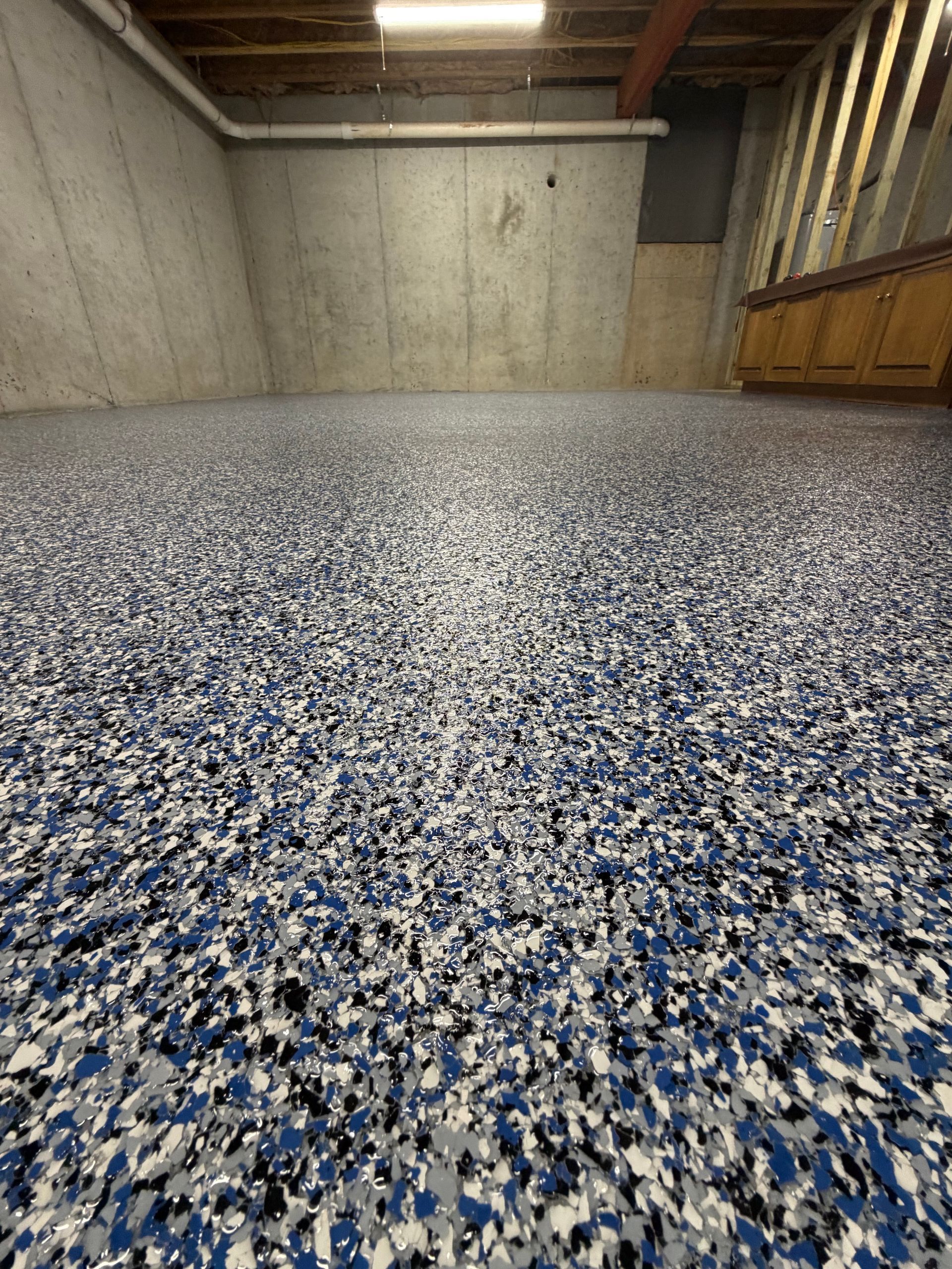 A basement room with a freshly coated floor featuring a blue, white, and black speckled epoxy finish against concrete walls.