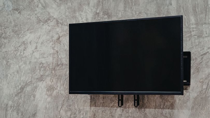 A black flat-screen television mounted on a textured, light gray concrete wall.