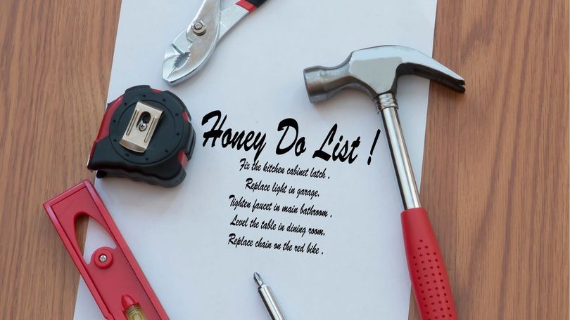 A Honey-Do list on paper surrounded by a hammer, tape measure, level, and pliers on a wooden surface.