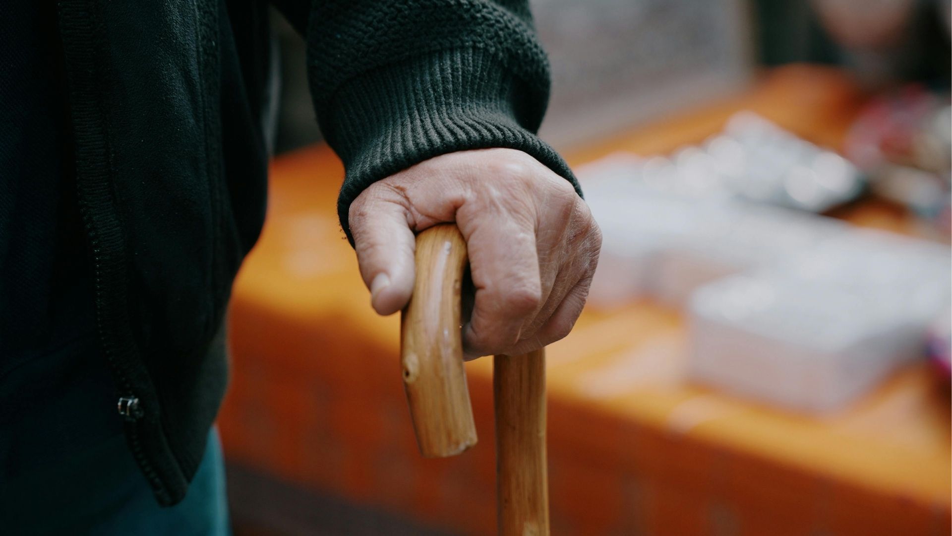 A person's hand grips the wooden handle of a walking cane.