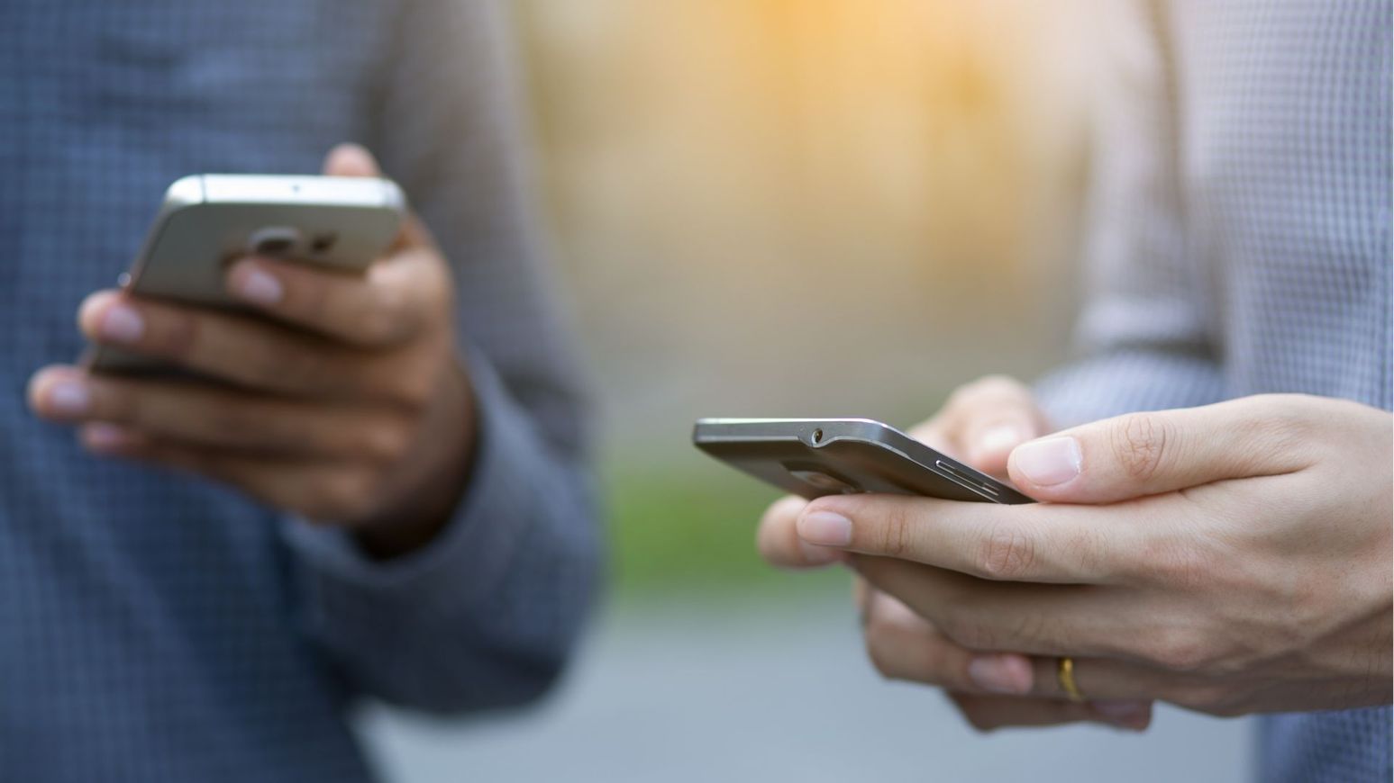 Two people hold and use smartphones, focusing on the devices in their hands.