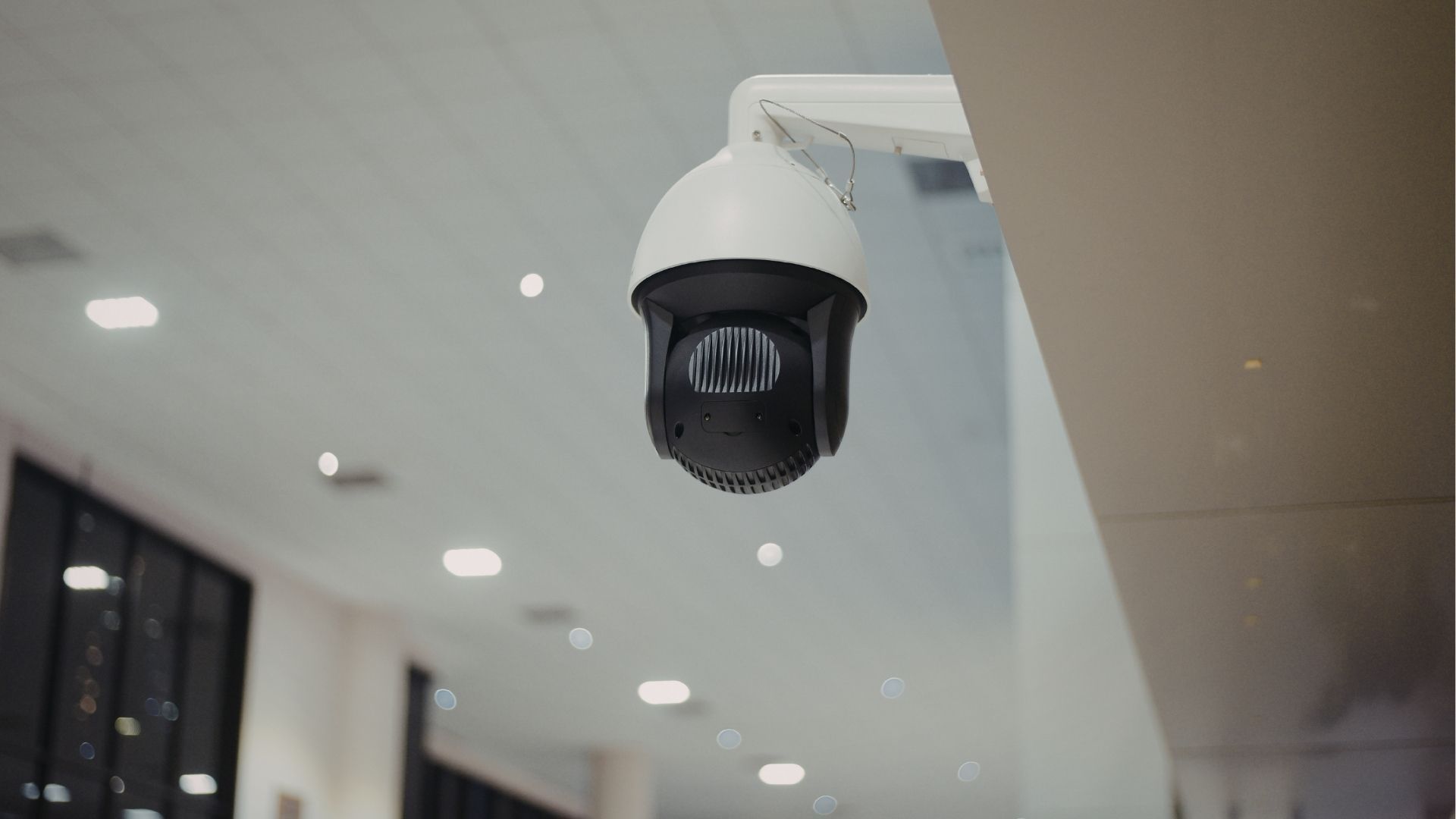 A white dome security camera is mounted on a ceiling corner inside a brightly lit indoor space.