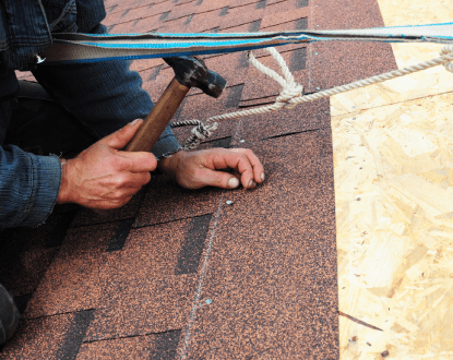 A man is hammering nails into a roof with a hammer.