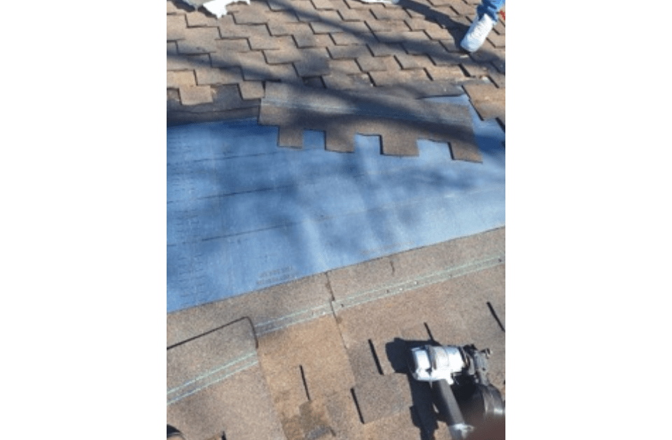 A person is laying shingles on a roof with a tool.