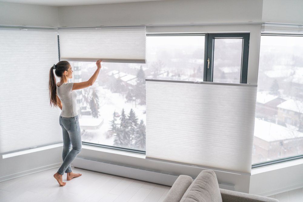 Woman opening home curtains in urban condo. Modern top down bottom up privacy cellular shades on apartment window keeping heat in winter with honeycomb blind curtain.