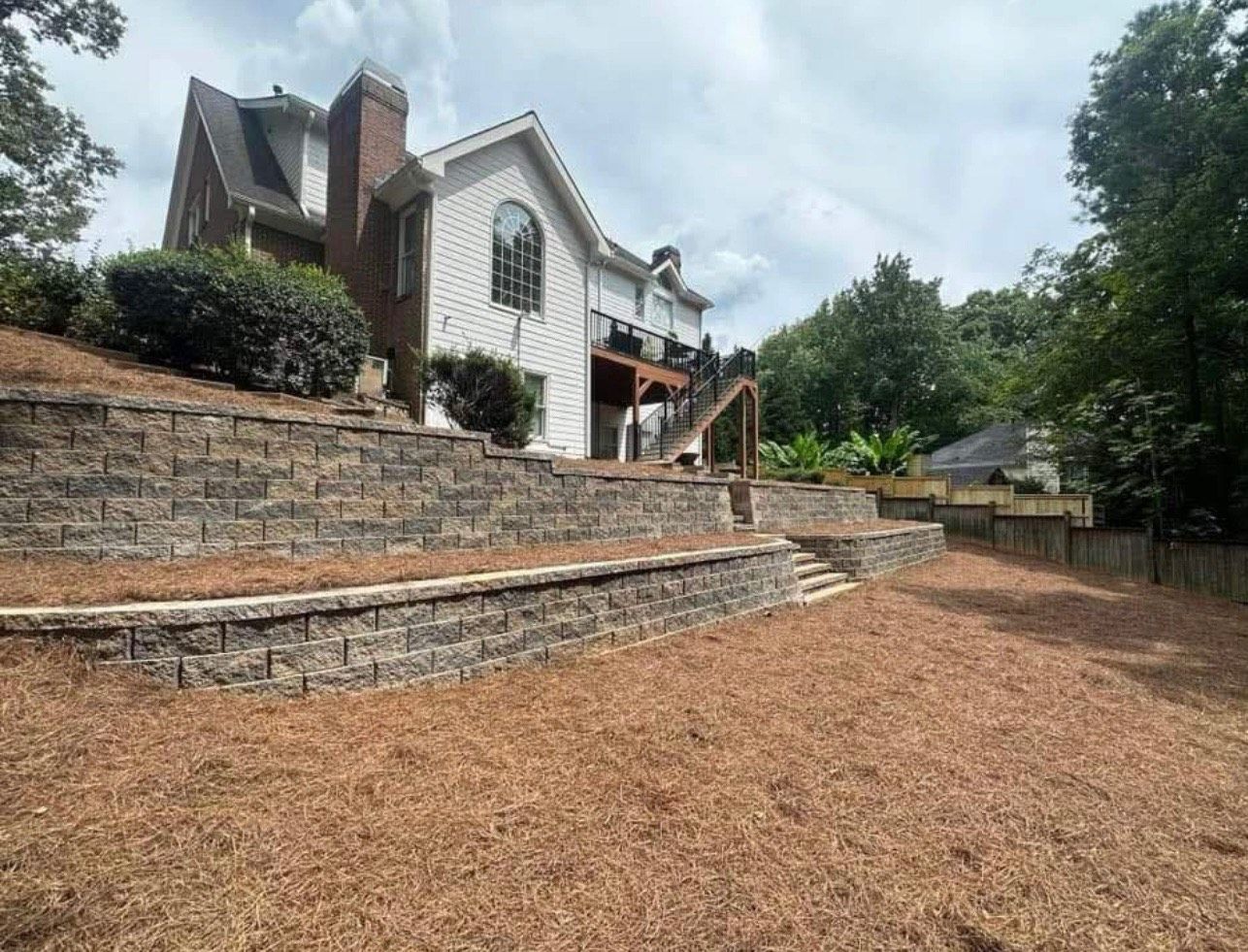 A large white house is sitting on top of a hill next to a brick wall.