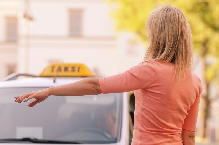 Woman in peach blouse waving taxicab