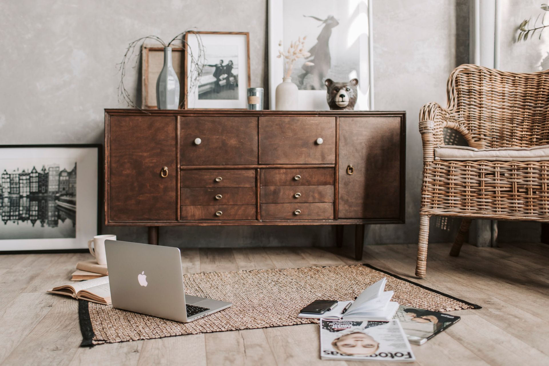 Wooden cabinet with decor, laptop, magazines, and wicker chair on a rug.
