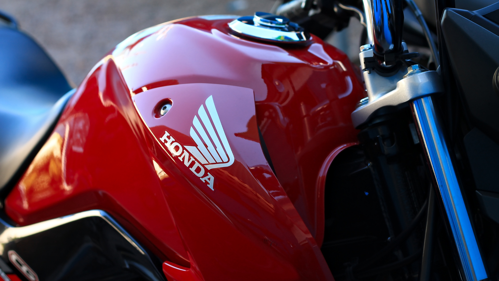 Close-up of a red Honda motorcycle fuel tank with logo and blue front fork.