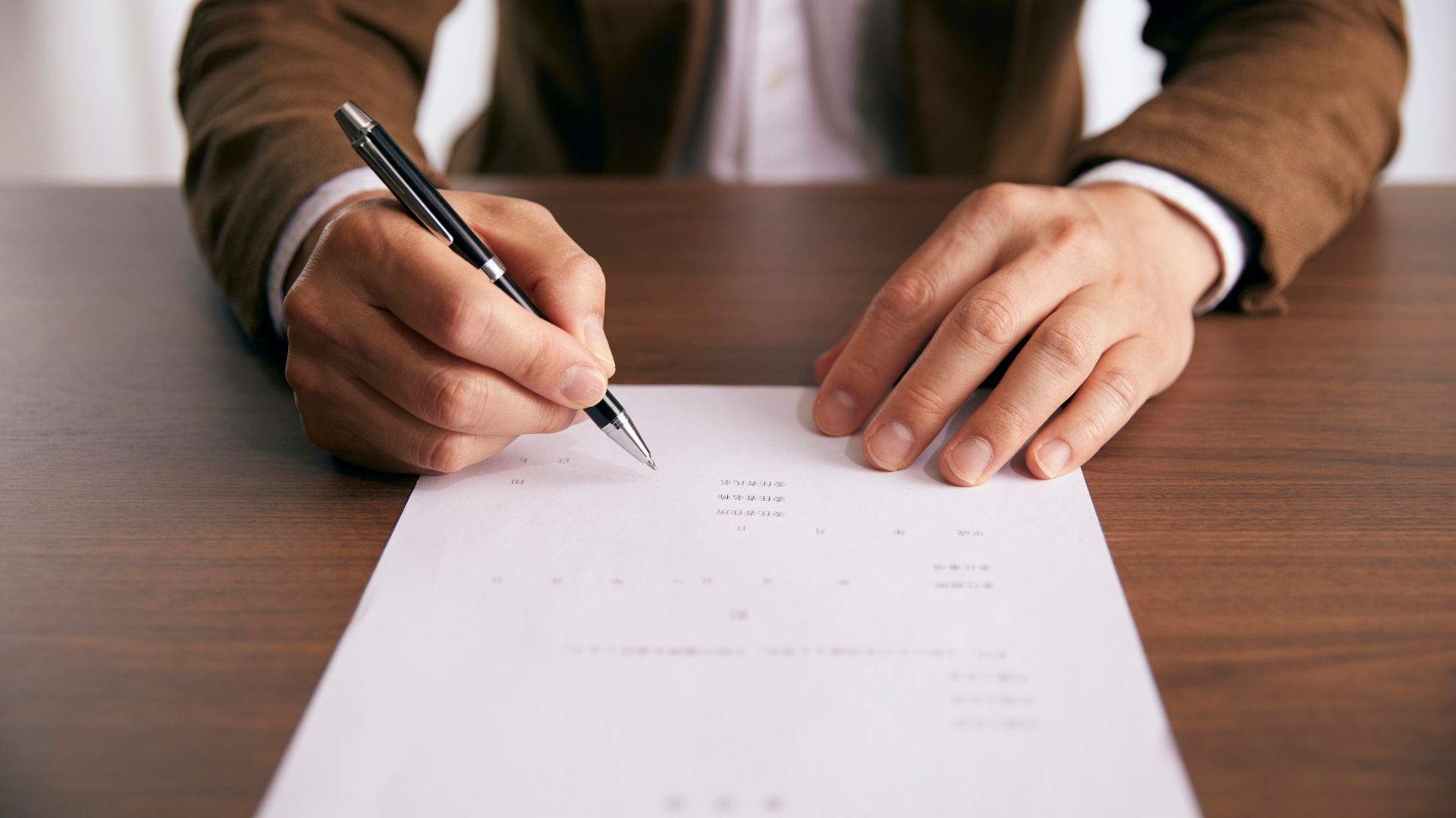 Hands signing a document on a desk with a black pen